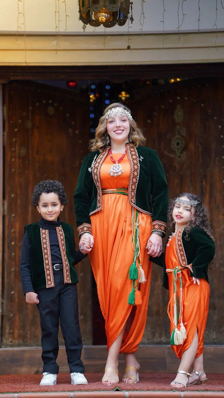 Femmes et enfants en vêtements traditionnels algériens orange avec vestes vertes, bijoux et décorations devant porte en bois
